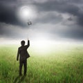 Business man holding bulb balloon in fields and raincloud Royalty Free Stock Photo