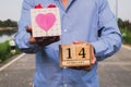 Business man holding 14 February wooden calendar and heart gift box. Valentine day concept