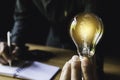 Business man holding light bulb on the desk in office and using  computer in  financial,accounting,energy,idea concept Royalty Free Stock Photo