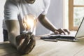 Business man holding light bulb on the desk in office and using  computer in  financial,accounting,energy,idea concept Royalty Free Stock Photo