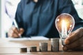 Business man holding light bulb on the desk in office and writing on note book it for financial,accounting,energy,idea concept Royalty Free Stock Photo