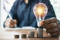 Business man holding light bulb on the desk in office and writing on note book it for financial,accounting,energy,idea concept Royalty Free Stock Photo
