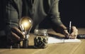 Business man holding light bulb on the desk in office and writing on note book it for financial,accounting,energy,idea concept Royalty Free Stock Photo