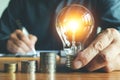 Business man holding light bulb on the desk in office and writing on note book it for financial,accounting,energy,idea concept.