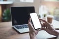 Business man holding mockup smartphone with blank white screen and computer laptop on wooden table in cafe shop Royalty Free Stock Photo