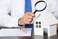 A business man looking at a model house holding a magnifying glass in his hand. Royalty Free Stock Photo