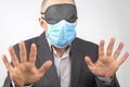 Business man in a medical mask and blindfold for sleeping with hands up on a white background