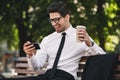 Business man outdoors in the park play games by phone drinking coffee. Royalty Free Stock Photo