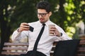 Business man outdoors in the park play games by phone drinking coffee. Royalty Free Stock Photo