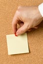 Business man pinning empty yellow sticky paper memo note on cork board