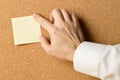 Business man pinning empty yellow sticky paper memo note on cork board