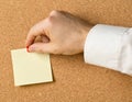 Business man pinning empty yellow sticky paper memo note on cork board