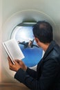 Business man reading book in passenger plane seat and looking to Royalty Free Stock Photo