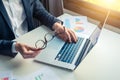 Business man with sight problem holding glasses and working on a laptop with graphic analysis charts Royalty Free Stock Photo