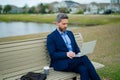 Business man sitting on a bench in park. Man is working on computer outside. Handsome business man making online work Royalty Free Stock Photo