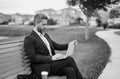 Business man sitting on a bench in park. Man is working on computer outside. Handsome business man making online work Royalty Free Stock Photo