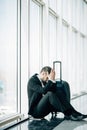 Business man sitting at the terminal airport on the floor with suitcase flight delay, two hands touch at head, headache, waiting t Royalty Free Stock Photo