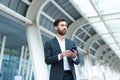 Business man standing background a modern train station airport or bus stop in formal suit with a suitcase using app mobile phone Royalty Free Stock Photo