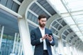 Business man standing background a modern train station airport or bus stop in formal suit with a suitcase using app mobile phone Royalty Free Stock Photo