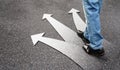 Business man standing on concrete floor with three arrows, left, right and front. Feet and white arrow sign on road. Different