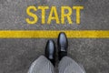 Business man standing on street background with word new start written. Pair of feet and black shoes on tarmac road with yellow Royalty Free Stock Photo