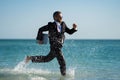 Business man in suit with laptop running in sea water. Travel tourism and business concept. Crazy male office employee