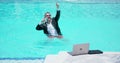 Business man in suit with laptop standing in the water in pool. Remote work. Crazy freelancer. Business and summer