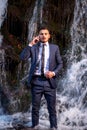 Business man in suit speaking with waterproof smartphone at waterfall background. IP68 device concept. Telework Royalty Free Stock Photo