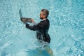 Business man in suit working on laptop in swimming pool. Travel tourism and business concept. Crazy male office employee