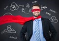 Business man superhero with hands on hips against navy chalkboard with white business doodles Royalty Free Stock Photo