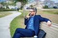 Business man talk on phone sitting on a bench in park. Man in suit call phone outside. Handsome business man using phone Royalty Free Stock Photo