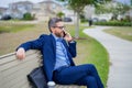 Business man talk on phone sitting on a bench in park. Man in suit call phone outside. Handsome business man using phone Royalty Free Stock Photo