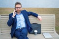 Business man talk on phone sitting on a bench in park. Man in suit call phone outside. Handsome business man using phone Royalty Free Stock Photo