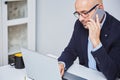 Business man teleworking from home with a laptop and talking on a cell phone. Bald man with glasses