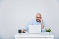 Business man teleworking from home with a laptop and talking on a cell phone. Bald man with glasses