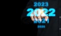 Business man touching a virtual image of New Year`s number 2022 in blue on a black background. Scenario of selection, search,