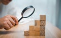 A business man uses a magnifying glass to look at the stacked wooden dice to find profits and investments.