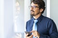 Business man wearing glasses looking through window holding his mobile phone sending voice message Royalty Free Stock Photo