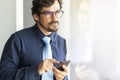 Business man wearing glasses looking through window holding his mobile phone texting Royalty Free Stock Photo