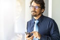 Business man wearing glasses looking through window holding his mobile phone texting Royalty Free Stock Photo