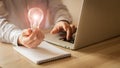 A business man wearing a gray shirt is sitting in front of a laptop holding a light bulb in his hand working technology ideas and Royalty Free Stock Photo