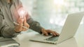 A business man wearing a gray shirt is sitting in front of a laptop holding a light bulb in his hand working technology ideas and Royalty Free Stock Photo