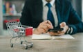 Business man wearing suit and calculates the budget. Shopping cart a on table with mobile. Budget of poor low income family. Royalty Free Stock Photo