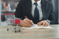 Business man wearing suit and calculates the budget. Shopping cart a on table with note book. Budget of poor low income family. Royalty Free Stock Photo