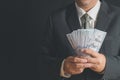 Business man wearing suit and necktie holding money in hand on black background, US dollar USD bills Royalty Free Stock Photo