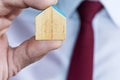 Business man with white  shirt and red tie holding a wooden miniature toy house in his finger Royalty Free Stock Photo