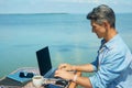 Business man working on the beach at morning by the sea, using laptop. Freedom, remote work, freelancer, technology Royalty Free Stock Photo