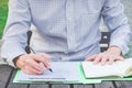 Business man writing notes in personal notebook with right hand, working in the park in front of office building Royalty Free Stock Photo