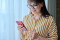 Business mature woman using smart phone standing in office near window Royalty Free Stock Photo