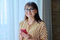 Business mature woman using smart phone standing in office near window Royalty Free Stock Photo